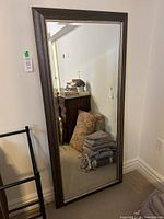 Full length view of a large rectangular standing mirror with gray and brushed nickel frame, placed leaning against the wall in a room.