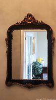 Full view of the ornate black and gold painted wood framed mirror hanging on the wall.