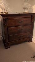 Full front view of the dark wood 3 drawer nightstand showing overall furniture piece, drawer layout, and carved detailing on corners.