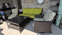 Overall view of wicker sofa, glass-top coffee table, swivel armchair and ottoman on covered patio