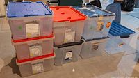 Stack of plastic storage containers with different colored lids including blue, red, and black, showing overall quantity and condition.