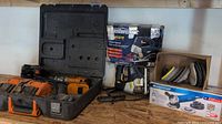 Rigid cordless drill in its black carrying case with charger and one battery, next to Mastercraft jigsaw in box, and Mastercraft angle grinder box with accessories.