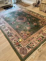 Full view of the green wool rug with central floral design and patterned border, showing overall condition and colors.