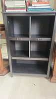 Front view of black floor standing shelf unit with five cubbies and metal label holders attached to horizontal dividers.