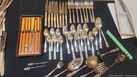 Full view of all flatware pieces including boxed fish knives with yellow handles on left, spoons laid out center, and serving utensils on right.