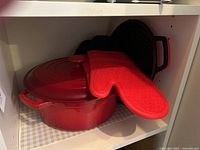 Overall view showing red Dutch oven with lid, grill pan behind and oven mitts on top