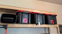Three black and red Craftsman 20 gallon storage containers placed on a wooden shelf in a garage environment.