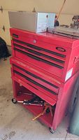 Red International 2-piece metal tool chest on casters with a silver accessory box on top and dry-wall saw to right