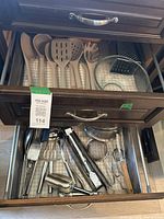 Two drawers shown; upper drawer contains silicone utensils with wooden handles, glass mixing bowls, and a metal handheld grater. Lower drawer contains multiple silver metal kitchen tools including strainers and scoops.