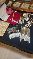 Overview photo displaying multiple sets of pearl handled cutting utensils and forks laid out on a table, including cutting knives, forks, and storage cases.