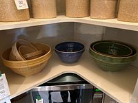 Photo showing the set of vintage stoneware mixing bowls: 4 tan/yellow bowls nested together on the left, 1 blue bowl in the middle, and 2 green bowls nested with square bottoms on the right.