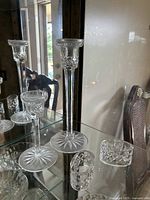 Photo showing both waterford crystal candlestick holders of different heights and two crystal napkin rings on a glass shelf with a mirrored backing.