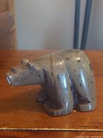 Side angle view of the hand-carved brown bear soapstone sculpture on wooden surface showing detail of the head, front leg, and body shape.