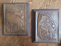 Photo of two wooden plaques side by side showing front carved designs of eagle on left and whale on right.