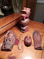 Top view showing the five wood carvings arranged on a wooden surface with the totem pole standing and the faces and paddle laying flat.