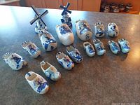 Photo showing entire collection of Dutch Delft blue pottery ashtrays shaped as traditional clogs and windmills, arranged on countertop.