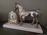 Photo showing the stallion electric clock on a smooth surface, with the clock face visible and the silver-tone horse figurine detailed in profile.