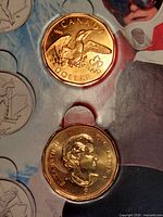 Close-up of two one-dollar Lucky Loonies showing the Maple Leaf, Queen Elizabeth II, and Olympic emblems
