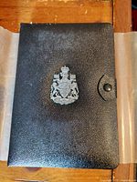 Closed black leatherette presentation book with Dominion of Canada crest on cover and clasp, housing the coin set.
