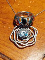 Close-up photo of the sterling silver ring with multiple dark stones around the band placed on top of a wavy silver pendant with a large clear gemstone.