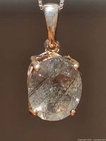 Close-up front view of oval rutilated quartz pendant in sterling silver setting showing needle-like rutile inclusions in quartz.