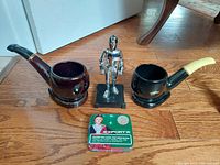 Photo showing two ceramic pipe ashtrays, flint & fluid knight lighter missing visor, and MacDonald Exporta cigarette tin.