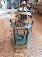 Front angle view of vintage brass hexagonal lantern with etched glass and metal handle on wood floor.