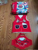 Photo showing folded patchwork colorful quilt and red vest with panda and floral embroidery, along with red apron with floral and coiled embroidered design.