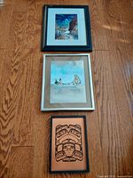 Photo showing all three framed foil artworks arranged vertically on floor, different sizes and framing styles, depicting First Nations imagery.