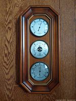 Front view of wood cased weather instrument showing humidity, barometer and thermometer dials.