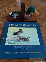 Front view of the 'From The Wild' portfolio book with painted mallard duck bookends on wooden bases.