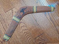 Handcrafted wooden boomerang with detailed Australian painted design including kangaroo motif, yellow and white dot patterns on curved wood, placed on wooden floor.