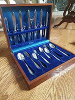 Opened mahogany box of silverplate flatware, showing knives, large spoons, forks and smaller spoons inside blue velvet lining.