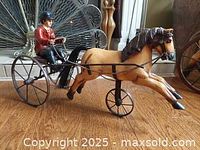 Profile view of vintage metal wheeled harness racer toy showing painted horse figurine and seated driver in red jacket on sulky cart with large rear wheels.