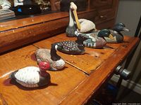 Angled side view of all six waterfowl miniatures arranged in a row on wood furniture surface.