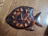 Top-down view of the vintage wood carved tropical fish quartz clock, showing detailed carvings and unique carved wooden number markers on a hardwood floor background.