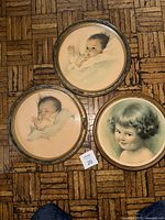 Three round framed prints laid on floor showing portraits of children, two frames with glass and one without