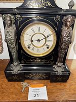 Front view of the Victorian Andonia mantel clock showing black and gold decorative details, round clock face, and two female figure accents on the sides.
