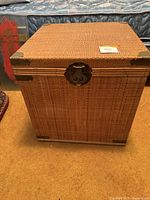 Front view of square wicker rattan trunk showing metal corner protectors and metal lock.