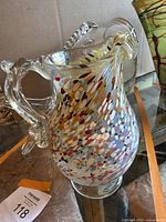 Colorful Murano art glass pitcher showing multicolor speckled pattern and clear glass handle and spout.