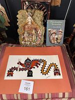 Photo showing Colombian ceramic nativity, Precolumbian pottery book, and one Native American style artwork mounted on orange mat