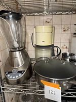 Photo showing Black & Decker blender, Braun coffee maker, and GreenPan frying pan with lid on a metal shelf