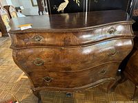 Front view of the burl wood chest, showing curved bombé style with three drawers and metal handles.