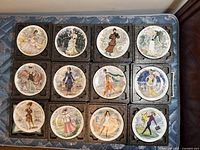 Top view of all 12 Darceau-Limoges collectible fashion plates arranged in four rows, showing various historical fashion styles.
