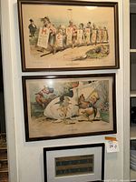 Three framed art pieces hanging on wall, two are large political cartoons, one smaller bottom print with B.C.