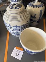 Photo showing two blue and white ginger jars, one with a lid, white porcelain with blue floral and geometric designs, some dirt or slight wear visible.