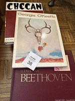 Five hardcover books stacked including a Georgia O'Keeffe art book, Beethoven music book, and other art/style books.