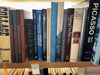 Shelf with a collection of hardcover art, architecture, and antiques books including titles such as 'Collage', 'The Illustrated Room', 'Picasso 1917-1926', and 'The Antiques Directory Furniture'.