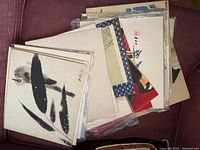 Stack of Japanese Sumi art prints showing a variety of traditional black ink brush paintings on paper, some with red stamps and abstract designs.