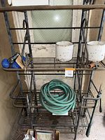 Full front view of the metal rack showing all items on it including buckets, garden hose, weights and sprayer.